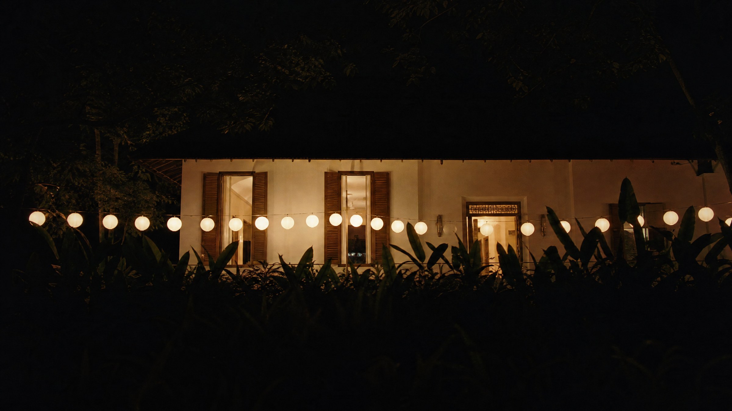 The garden terrace above the beach after dark, strung with lit paper lanterns.