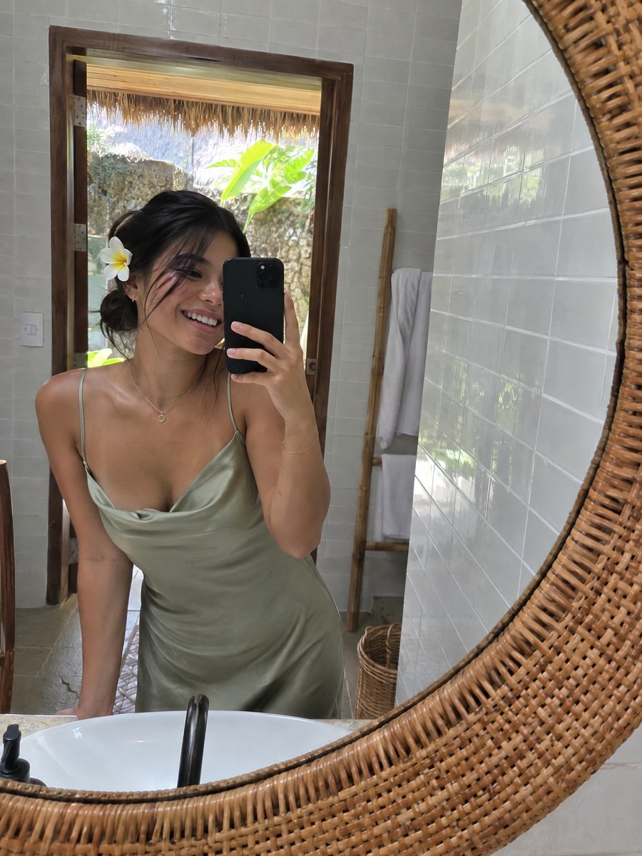 A guest in a sage dress taking a mirror selfie, a frangipani behind her ear.