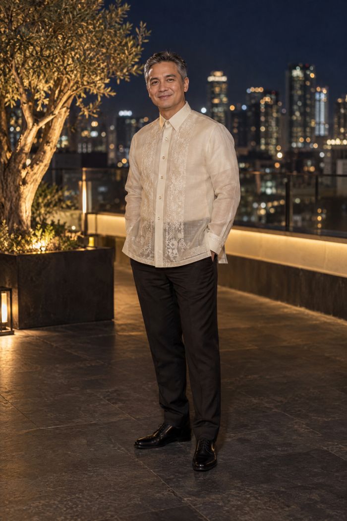 A man in a piña-silk barong with fine embroidery over black trousers, on the roof at night.