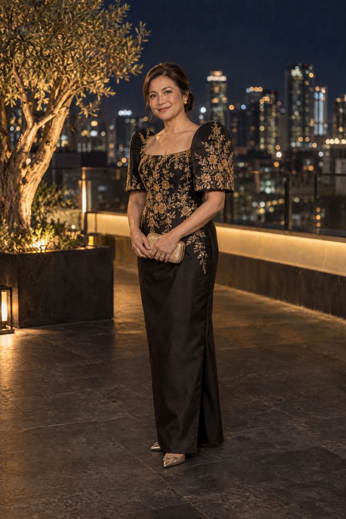 A woman in a black terno with butterfly sleeves and gold embroidery, holding a small gold clutch.