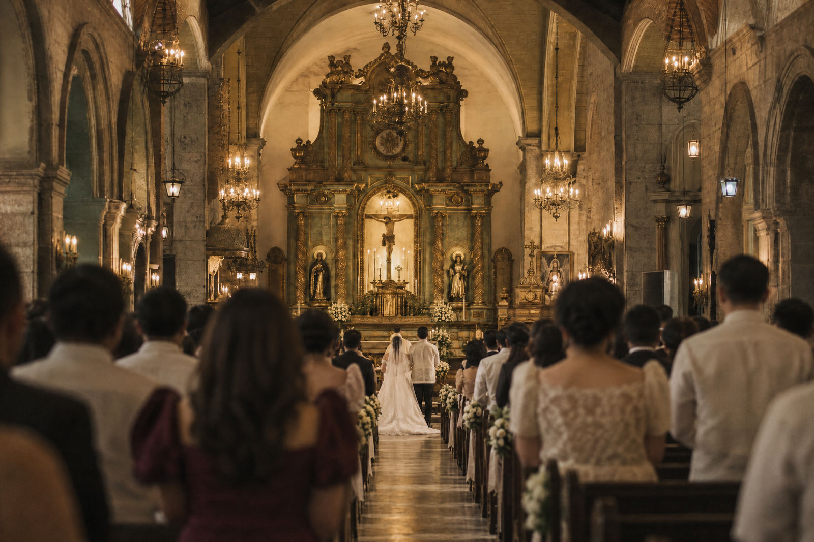 The processional seen from the back of the nave, the bride on her father’s arm far down the aisle between full pews.