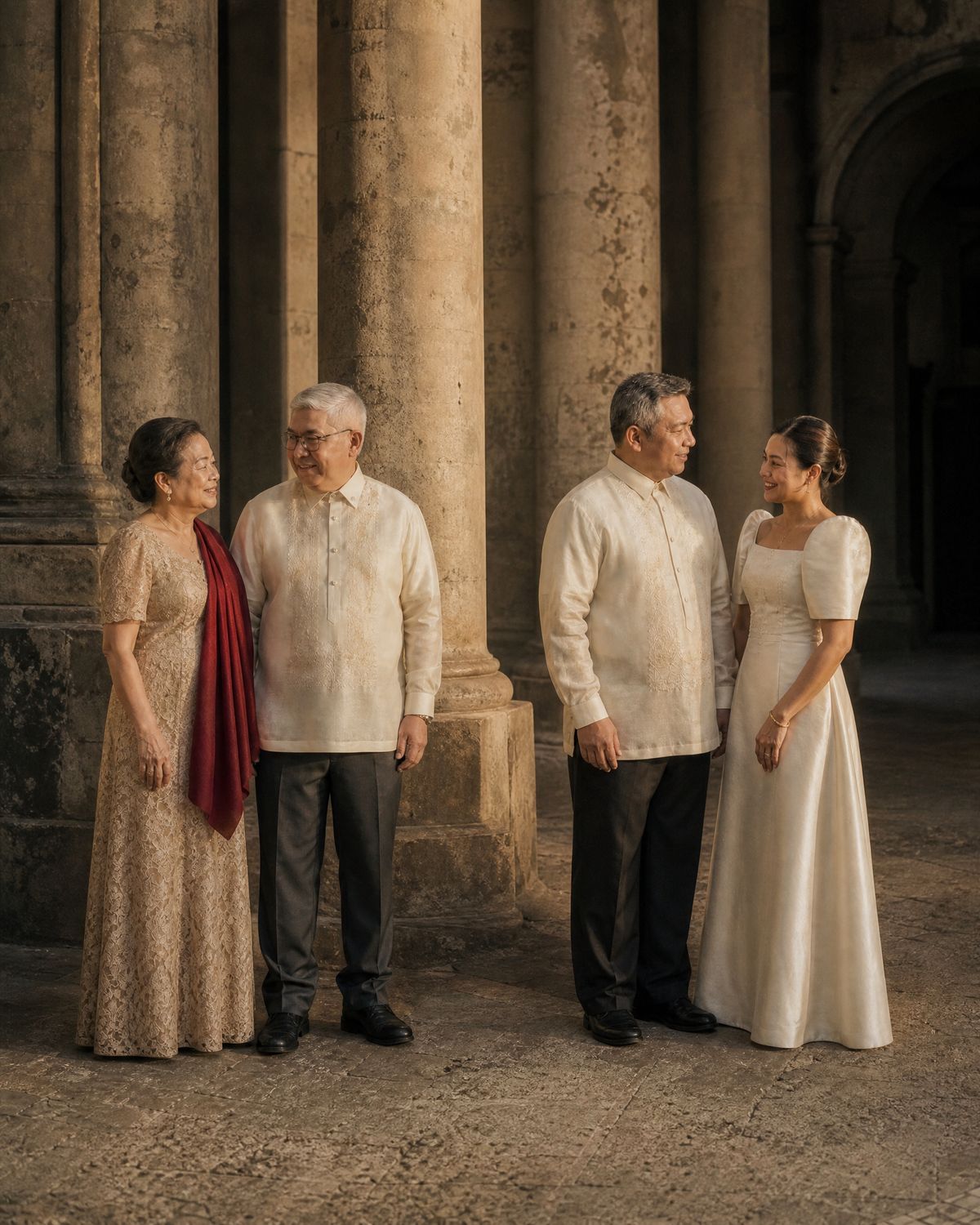 Two married couples in formal Filipiniana standing as pairs in the church portico before the ceremony, the fathers in ivory barong, one of the mothers wearing a deep red shawl.