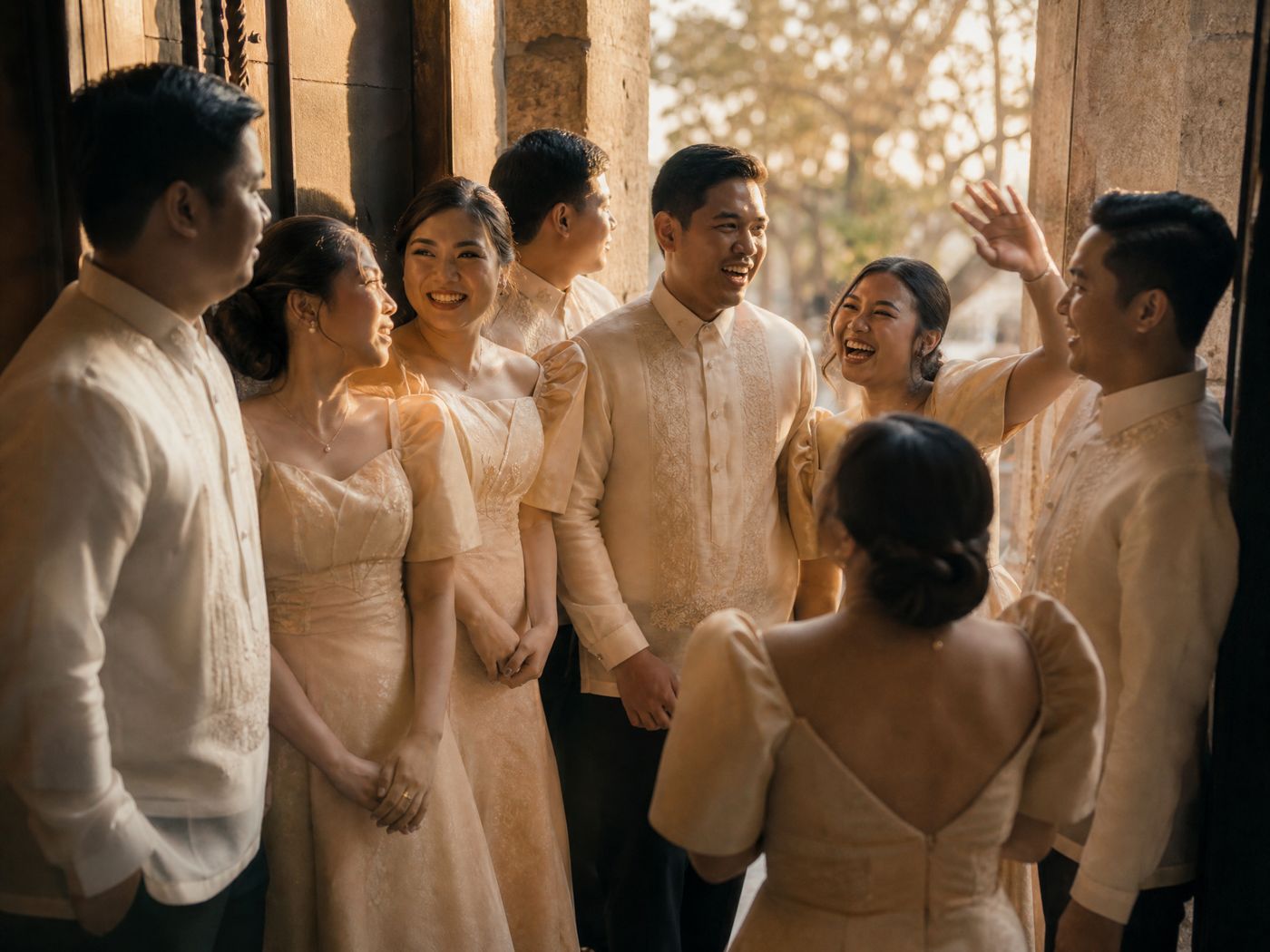 Eight friends in formal Filipiniana crowded into a stone doorway, all of them laughing at something out of frame.
