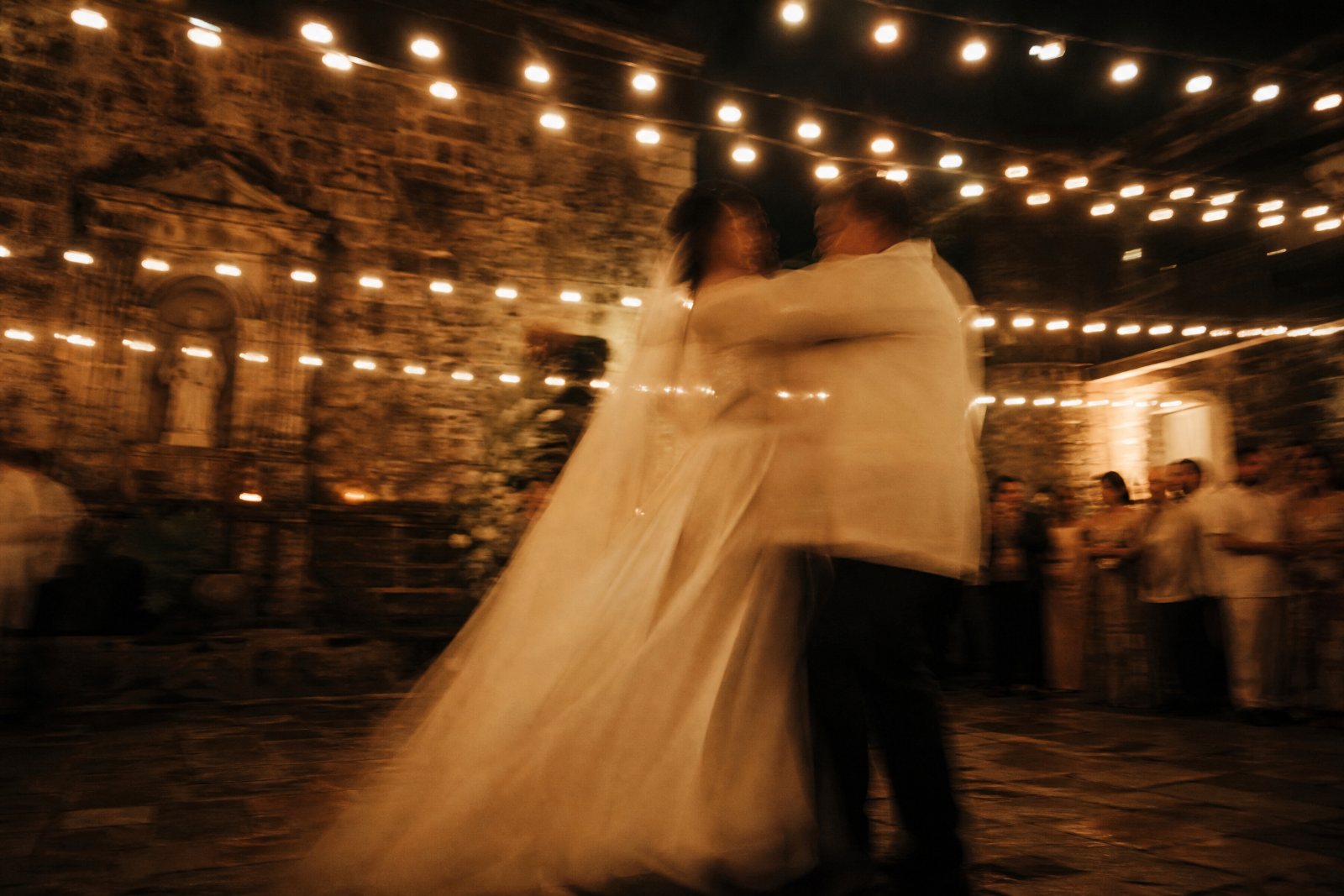 A motion-blurred last dance under courtyard lights.