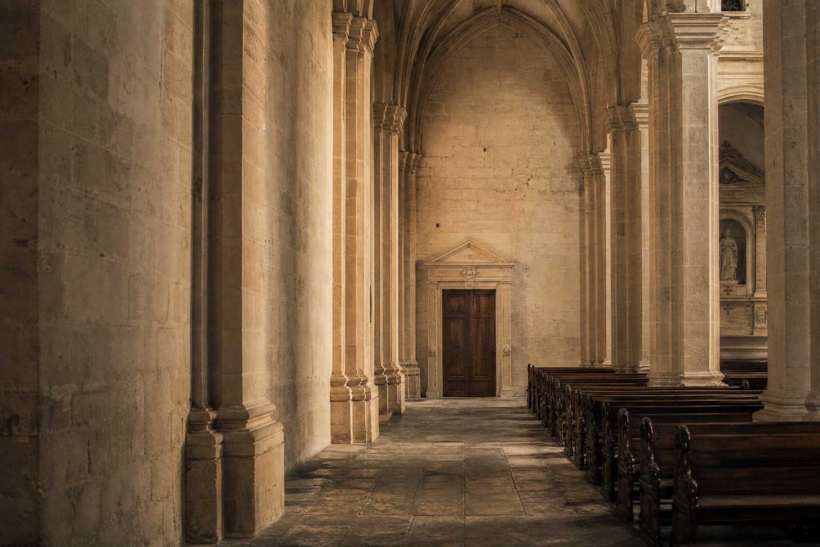 The stone side aisle of the parish, columns on one side and empty pews on the other.