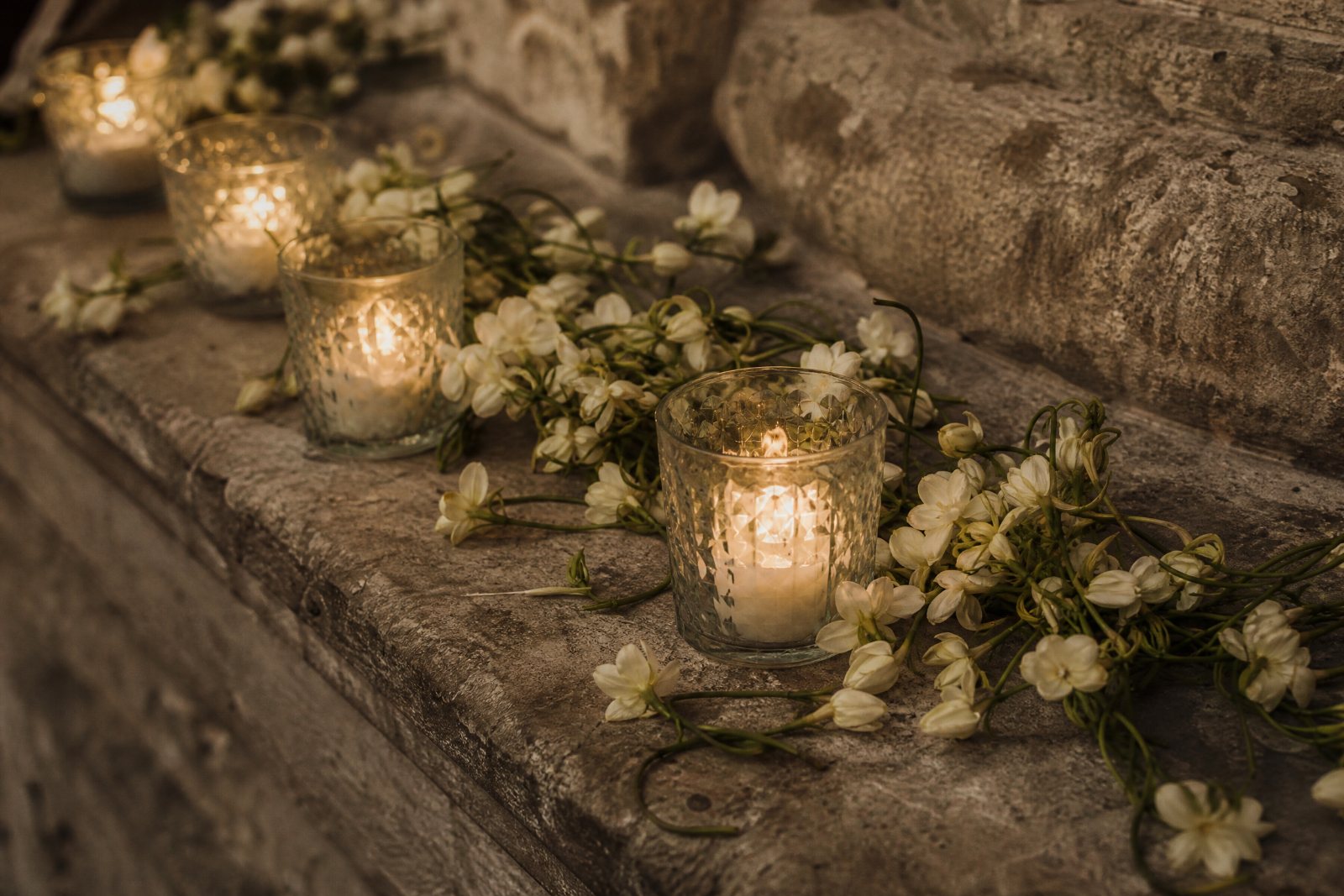 Candles and strands of sampaguita arranged on a stone ledge.