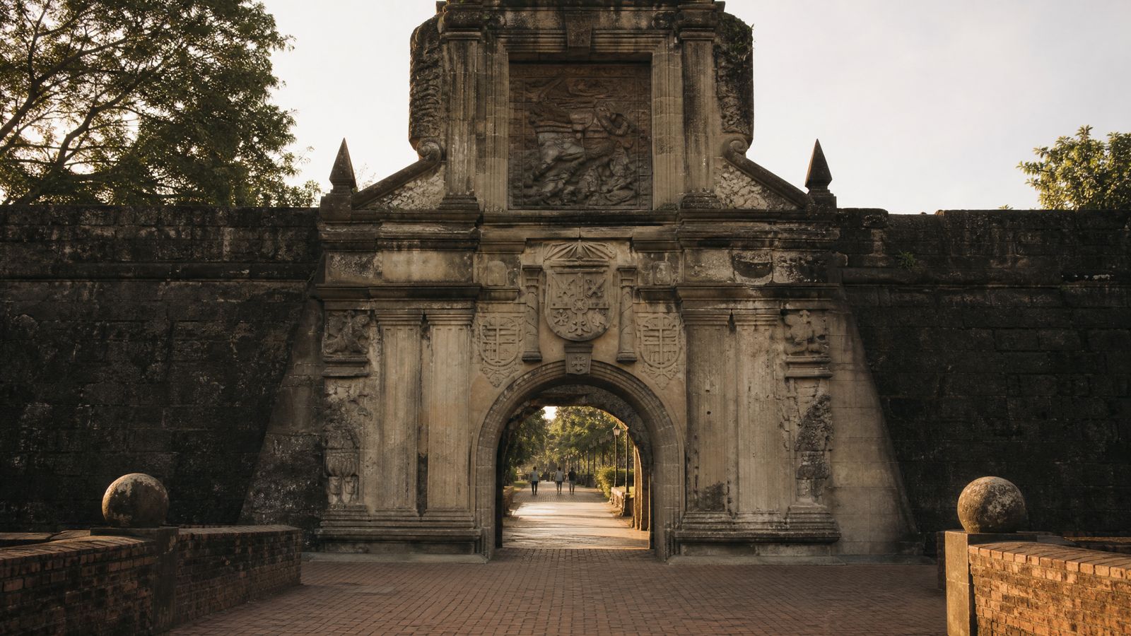 A Spanish-colonial stone gateway into the walled city photographed from outside in early morning light, the road passing through the arch into shadow and out into sun.