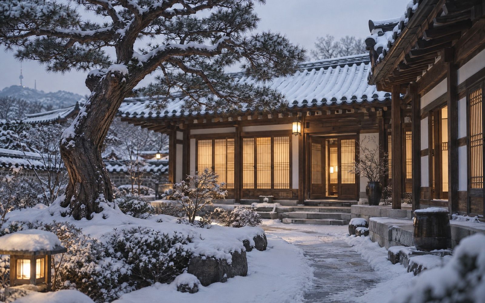 A hanok courtyard at blue hour, snow on the roof tiles and an old pine, paper-screen doors lit warm from inside.