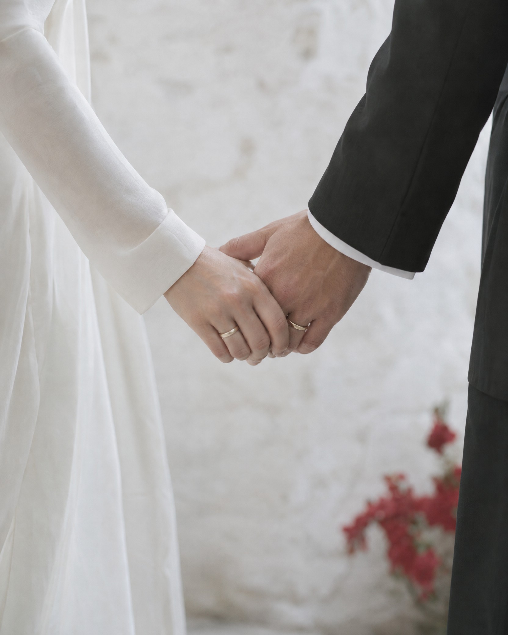 Their joined hands at the ceremony, an ivory sleeve and a black cuff, two plain gold bands.