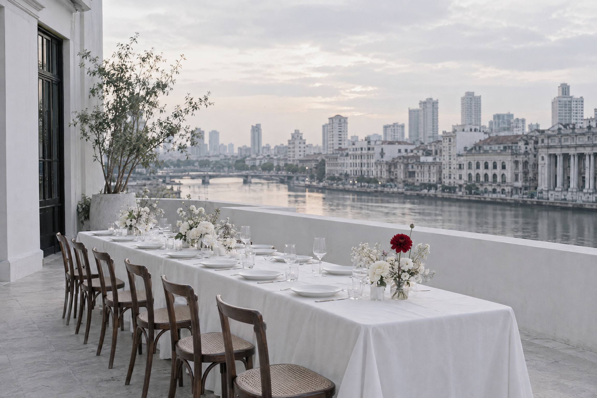 One long white table along the roof parapet at dusk, the river behind it.