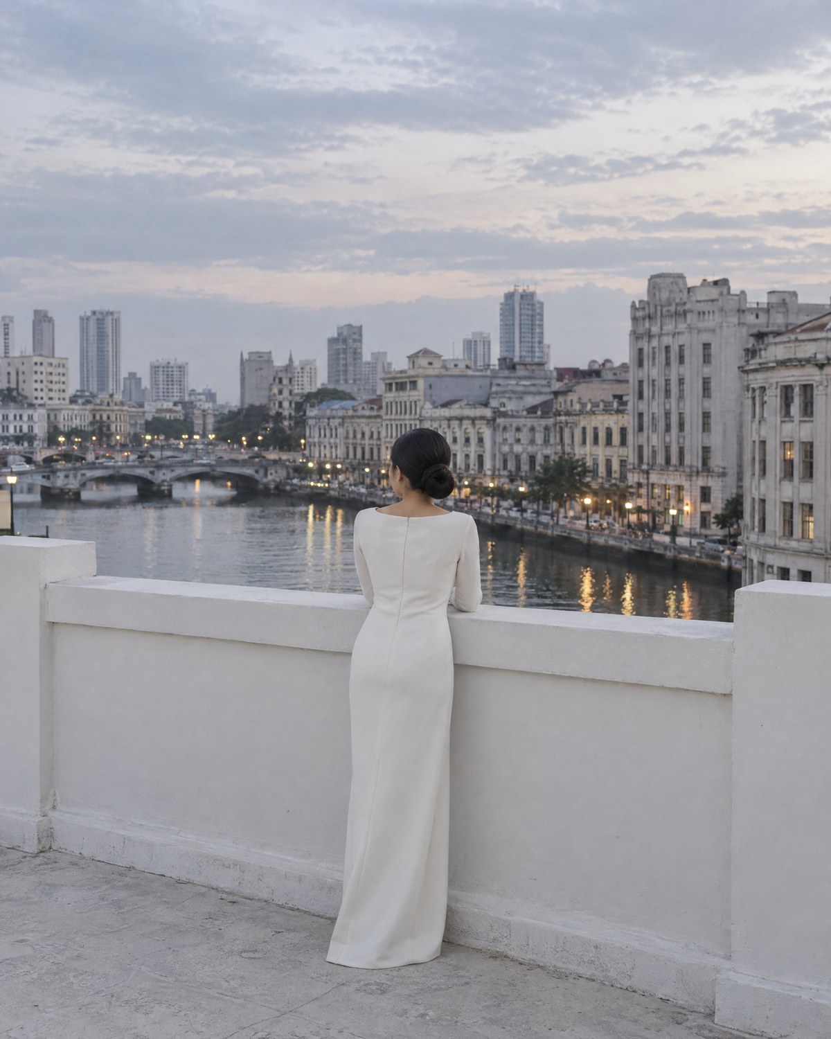 Ysabel alone at the roof parapet in the blue evening light, looking out over the old city.